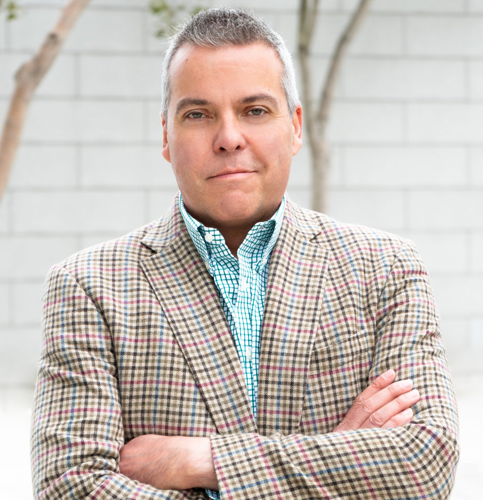 A man in a plaid jacket standing in front of a tree.