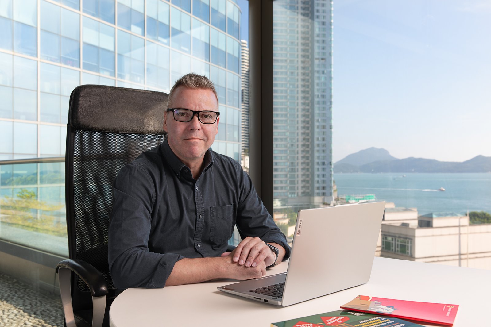 A man sitting at a desk with a laptop in front of a window.